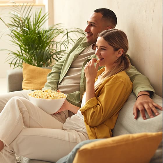 Young couple relaxing on the sofa, watching TV and eating pop corn.